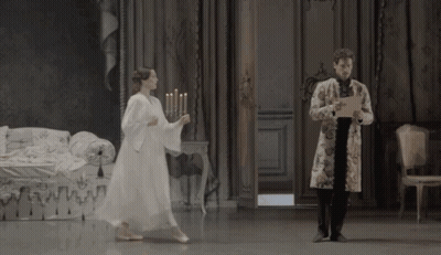 A Man Holding A Piece Of Paper Stands Next To A Woman In A White Dress Holding Candles GIF