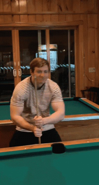 A Man Holding A Pool Cue On A Pool Table In Front Of A Window With The Number 00 On It GIF