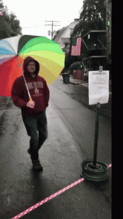 A Man Holding A Rainbow Colored Umbrella Is Wearing A Sweatshirt That Says ' Boston ' On The Front GIF