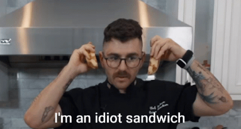 A Man Holding A Sandwich With The Words I 'M An Idiot Sandwich Written Below Him GIF