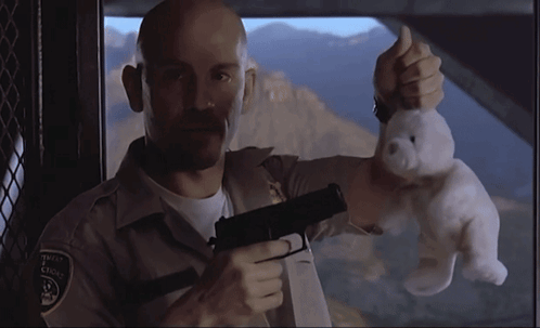 A Man Holding A Teddy Bear And A Gun With A Patch On His Chest That Says ' Sheriff ' On It GIF