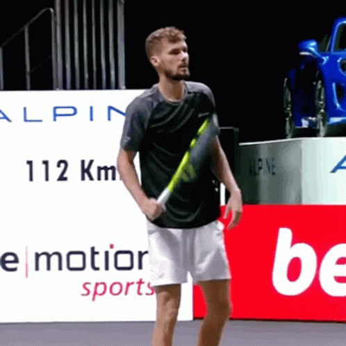 A Man Holding A Tennis Racquet In Front Of A Sign That Says ' Motion Sports ' GIF