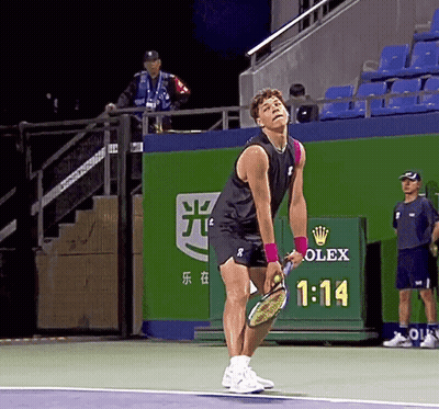 A Man Holding A Tennis Racquet On A Tennis Court With A Rolex Sign Behind Him GIF