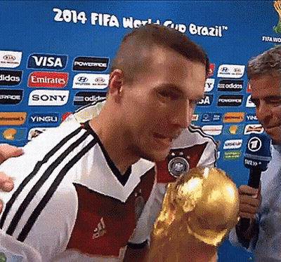 A Man Holding A Trophy In Front Of A 2014 Fifa World Cup Brazil Banner GIF