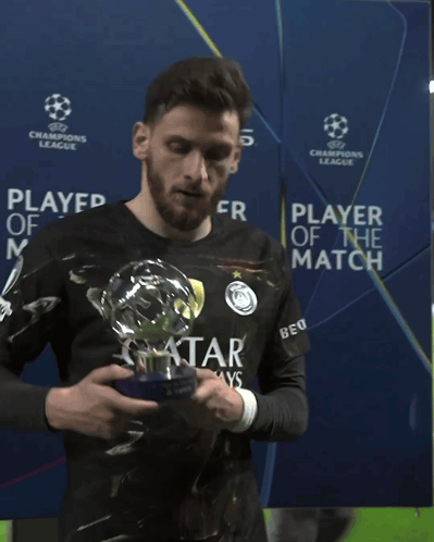 A Man Holding A Trophy In Front Of A Champions League Banner GIF