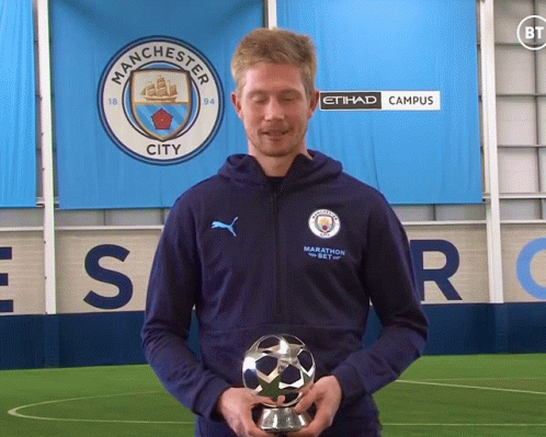 A Man Holding A Trophy In Front Of A Manchester City Sign GIF