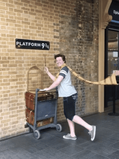 A Man Holding A Wand In Front Of A Sign That Says Platform 9 3/4 GIF