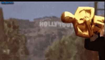 A Man Holding An Oscar Statue In Front Of A Hollywood Sign GIF