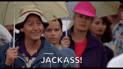 A Man Holding An Umbrella Says Jackass In A Crowd GIF