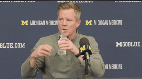 A Man Holds A Bottle Of Water In Front Of A Michigan Medicine Logo GIF
