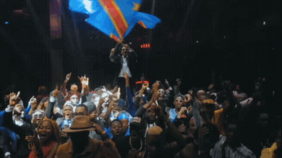 A Man Holds A Flag In Front Of A Crowd Of People GIF