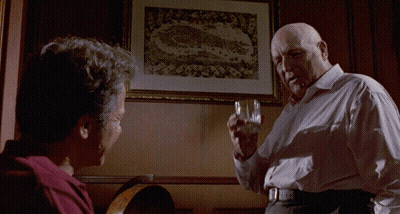 A Man Holds A Glass In Front Of A Framed Picture That Says Juicy GIF