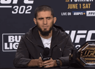 A Man Holds A Microphone In Front Of A Ufc Championship Belt GIF