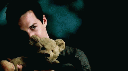 A Man Holds A Teddy Bear In Front Of His Face In A Dark Room GIF