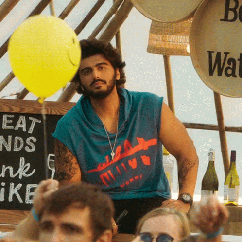 A Man Holds A Yellow Balloon In Front Of A Sign That Says Eat And Drink GIF