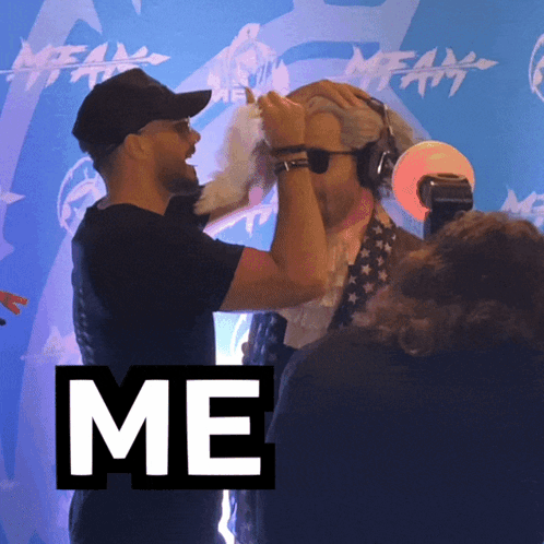 A Man Holds Another Man 'S Head In Front Of A Blue Wall With The Word Me On It GIF