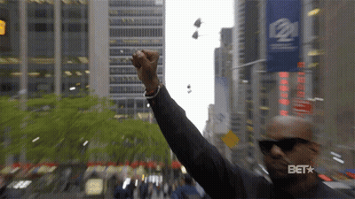 A Man Holds His Fist Up In The Air In Front Of A Sign That Says Bet GIF