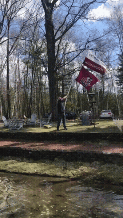 A Man Holds Up A Flag That Says Massachusetts On It GIF