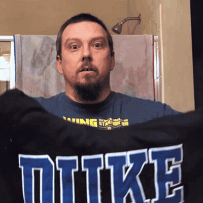 A Man Holds Up A Shirt That Says Duke GIF