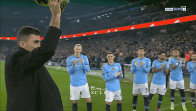 A Man Holds Up A Soccer Ball In Front Of A Group Of Soccer Players Wearing Blue Shirts With The Word City On Them GIF