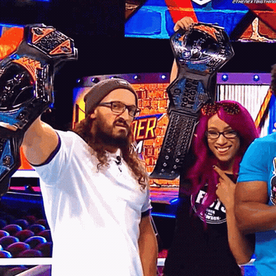 A Man Holds Up Two Championship Belts While Standing Next To A Woman GIF