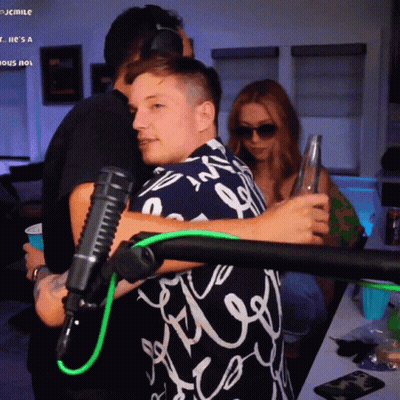 A Man Hugging Another Man In Front Of A Microphone That Says Jcmile On The Bottom Right GIF