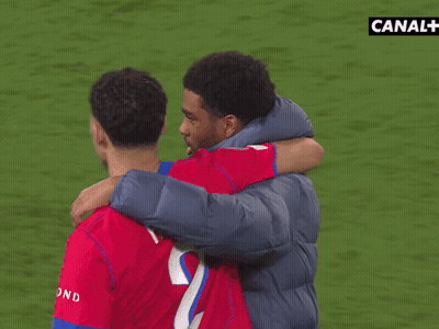 A Man Hugging Another Man On A Soccer Field With Canal + In The Background GIF