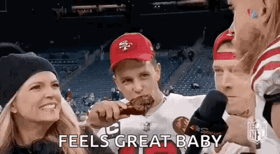 A Man In A 49Ers Hat Is Eating A Piece Of Meat While A Woman Holds A Child . GIF