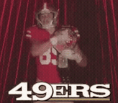 A Man In A 49Ers Jersey Is Standing In Front Of A Red Curtain GIF