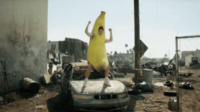 A Man In A Banana Costume Is Standing In Front Of A Broken Car . GIF