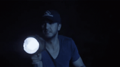 A Man In A Baseball Cap Holds A Flashlight GIF