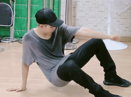 A Man In A Baseball Cap Is Sitting On The Floor With His Legs Crossed GIF