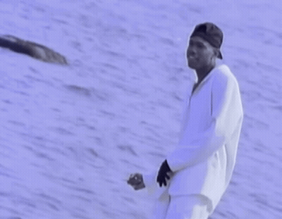 A Man In A Baseball Cap Is Standing In Front Of A Body Of Water GIF