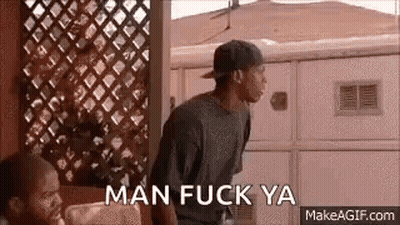 A Man In A Baseball Cap Is Standing In Front Of A Fence With The Words `` Man Fuck Ya '' . GIF