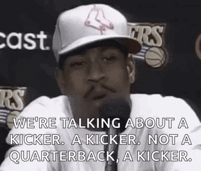 A Man In A Baseball Cap Is Talking Into A Microphone While Wearing A White Shirt . GIF