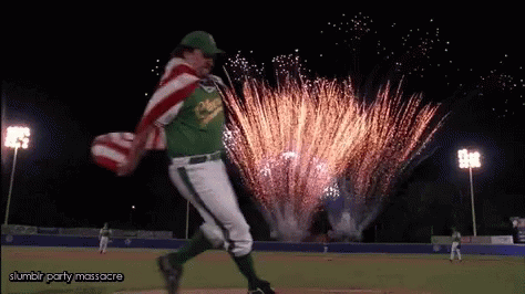A Man In A Baseball Uniform Is Running With An American Flag In Front Of Fireworks .. GIF