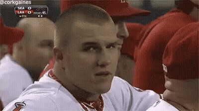 A Man In A Baseball Uniform Is Sitting In A Dugout Looking At The Camera . GIF
