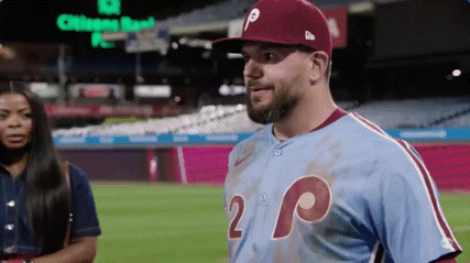 A Man In A Baseball Uniform Is Standing On A Baseball Field With A Woman In The Background . GIF