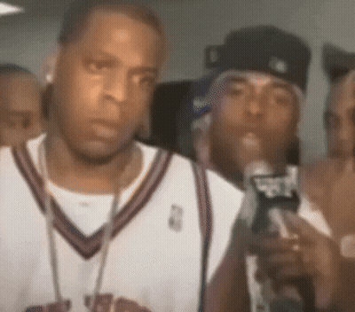 A Man In A Basketball Jersey Is Holding A Microphone In Front Of A Crowd . GIF