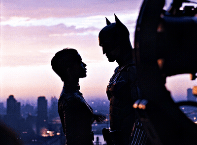 A Man In A Bat Suit Stands Next To A Woman In A Silhouette GIF