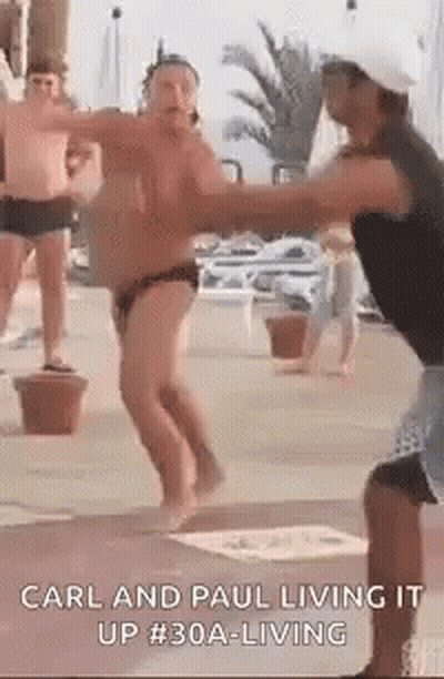 A Man In A Bathing Suit Is Dancing With Another Man In A Hat . GIF