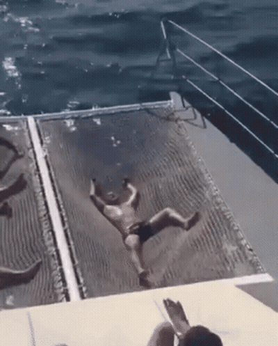 A Man In A Bathing Suit Is Falling Into The Ocean From A Boat . GIF