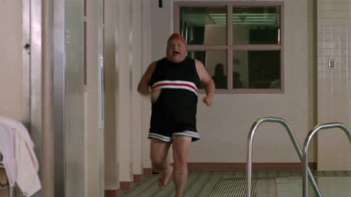 A Man In A Bathing Suit Is Running In A Hallway GIF