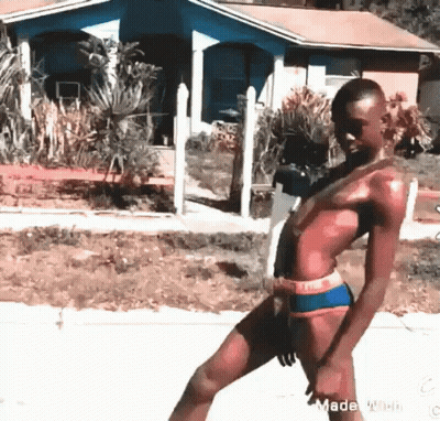 A Man In A Bathing Suit Is Walking Down A Street In Front Of A House . GIF