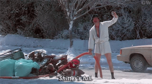 A Man In A Bathrobe Is Standing In The Snow Holding A Vacuum Cleaner And A Bottle . GIF