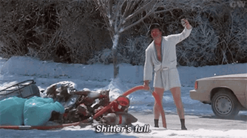 A Man In A Bathrobe Is Standing In The Snow Next To A Car And Holding A Bottle Of Beer . GIF