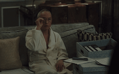 A Man In A Bathrobe Sits On A Couch With A Pillow GIF