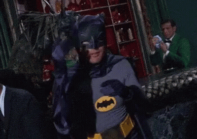 A Man In A Batman Costume Covers His Eyes With His Hands GIF