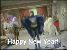 A Man In A Batman Costume Is Dancing In Front Of A Group Of People With The Words Happy New Year . GIF