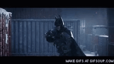 A Man In A Batman Costume Is Holding Another Man In A Dark Room . GIF
